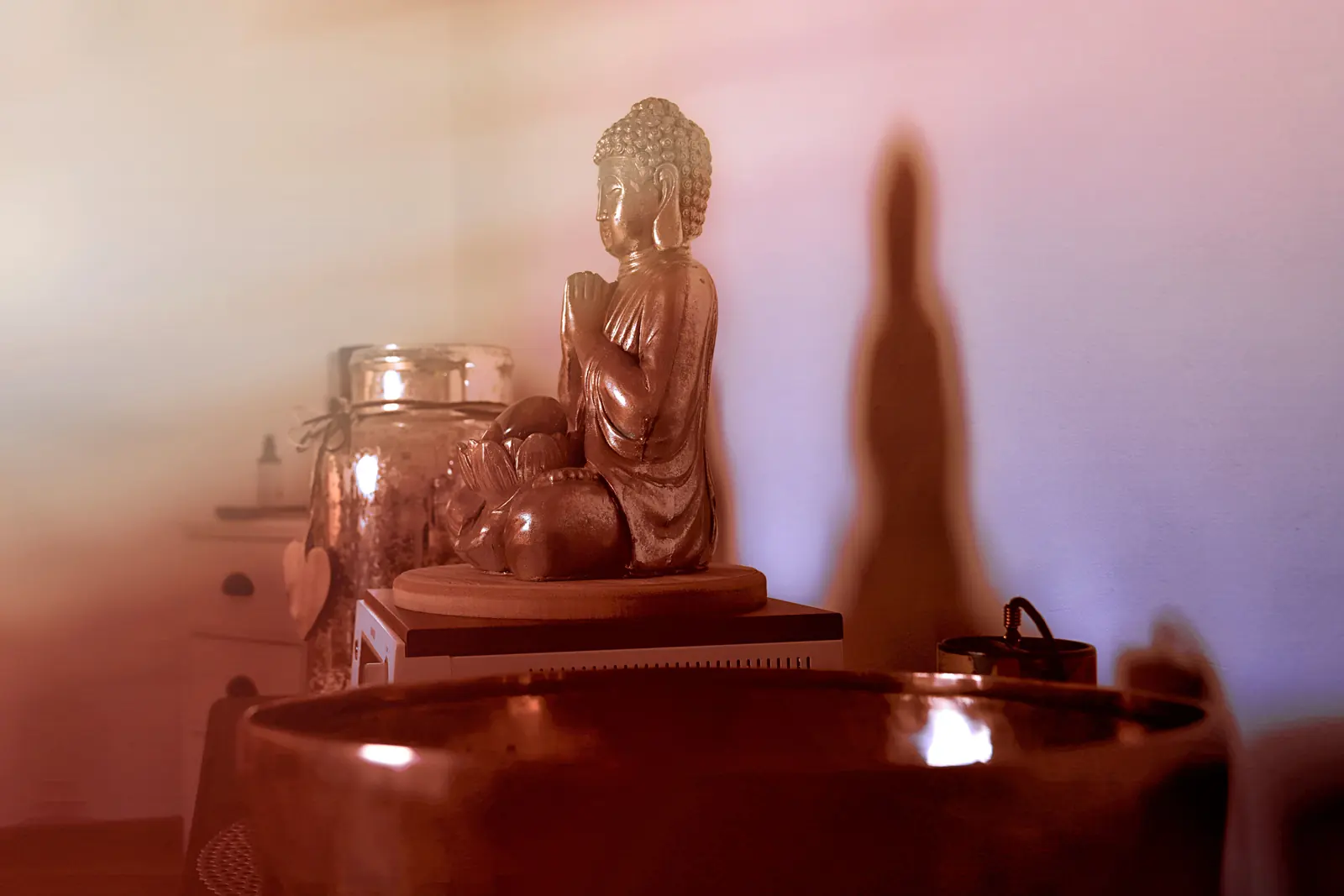 Kupferne Buddhafigur in warmem Licht, davor der Rand einer Klangschale